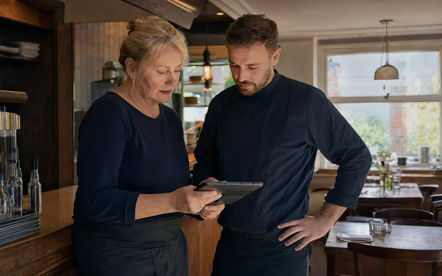 Gastronomin und jüngerer Mitarbeiter organisieren Reservierungen gemeinsam am Tablet